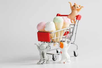 Three cute toy kittens with raised paws and a supermarket cart filled with ice cream in waffle...