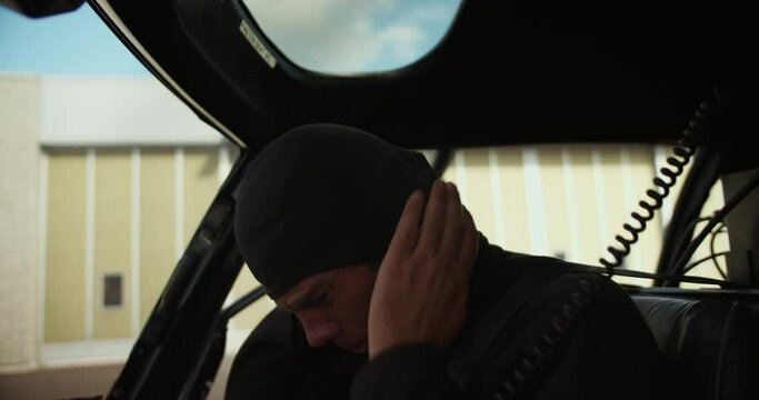 Mid adult Caucasian man putting helmet on head. Pilot performing preflight procedure in helicopter cockpit. Airport and aviation concept