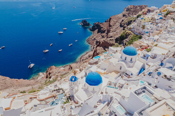 Panorama of Greek Orthodox Churc with blue dome and blue vibrant sea. Aerial view Santorini, Greece.