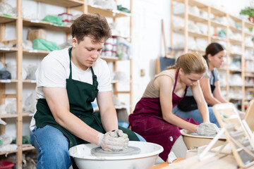 Young woman teacher in apron shows students teenage girl and teenage boy how to sculpt ceramic...