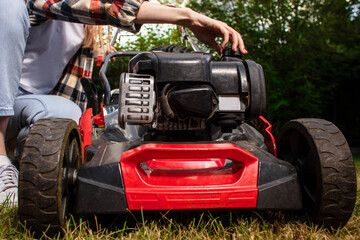 Obraz premium Concept of gardening, work, nature. Housework, gardening and country life. Home garden grass cutting woman mowing with lawn mower. Detail of lawn mower. Сutting grass in backyard. 