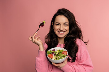Waist-up portrait of a pleased lady eating a portion of an appetizing vegetable salad with the fork...