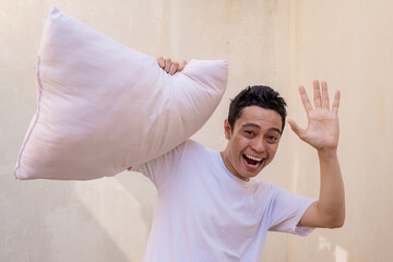 Indonesian man pose and gesture when pillow fight with friend, with happy expression. The photo is suitable to use for man expression advertising and fashion life style.