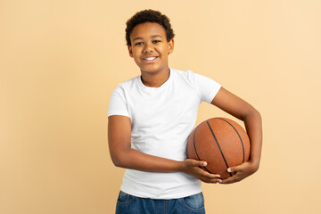 Portrait of young smiling African American boy holding ball playing basketball isolated on background. Sport, hobby, healthy lifestyle concept