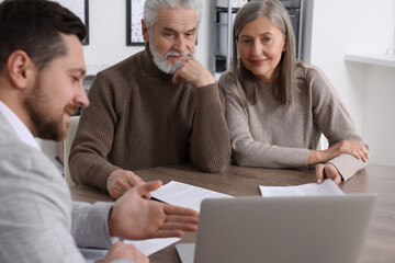 Elderly couple consulting insurance agent about pension plan at wooden table indoors