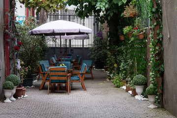 Street summer cafe in Tbilisi. Table, blue wooden chairs, white umbrella in European courtyard. Greenery on gray stone wall. Flowerbed with flowers. Concept of food, vacation, tourism, lunch, dinner