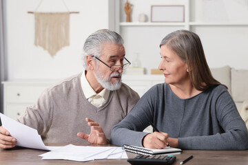 Elderly couple with papers discussing pension plan at wooden table indoors