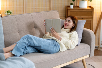 young woman lying on the sofa reading a book or a note that looks