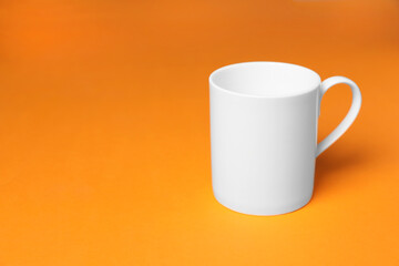 One white ceramic mug on orange background, space for text
