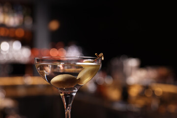 Martini glass with fresh cocktail and olives against blurred background. Space for text