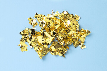 Many pieces of edible gold leaf on light blue background, top view