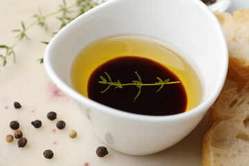 Bowl of organic balsamic vinegar with oil, spices and bread slices on beige table, closeup