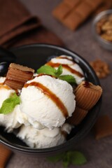 Bowl of tasty ice cream with caramel sauce, candies and mint on brown table, closeup
