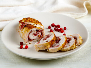 slices of delicious barbecue chicken or turkey roulade stuffed with cranberry on white dish on white wooden table, top view from above, close-up