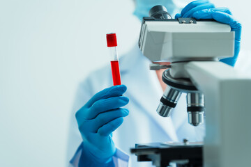 Close up dedicated hematology lab technician scrutinizing blood sample analysis under microscope, scientific laboratory research and drug testing concept, red color liquid