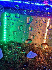 Waterdrops on glass surface reflecting a colorful textured bright background.