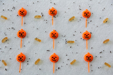 Halloween patterned background with pumpkin food picks and gummies candies on white textured background. 