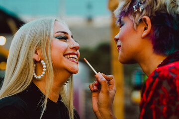 Young woman smiling as her friend applying lipstick on her.