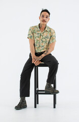 Isolated cutout studio full body shot Asian vintage classic male fashion model with mustache neck arm tattoo wearing eyeglasses in casual outfit posing sitting on chair on white background