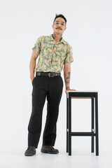 Isolated cutout studio full body shot Asian vintage classic male fashion model with mustache neck arm tattoo wearing eyeglasses in casual outfit standing near chair with boots on white background