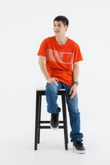 Portrait isolated cutout studio shot Asian smart handsome male fashion model in fashionable casual outfit t shirt blue jeans and sneakers sitting posing on chair look at camera on white background