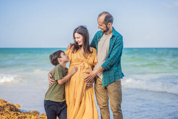 A loving family enjoying tropical beach - a radiant pregnant woman after 40, embraced by her husband, and accompanied by their adult teenage son, savoring precious moments together amidst nature's