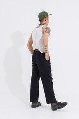 Isolated cutout studio shot Asian vintage classy mustache with neck arms hands tattoos male fashion model in casual fashionable sleeveless shirt cap boots posing standing on white background.