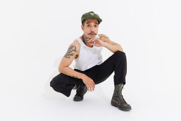 Isolated cutout studio shot Asian vintage classy mustache with neck arms hands tattoos male fashion model in casual fashionable sleeveless shirt cap boots sitting on floor on white background.