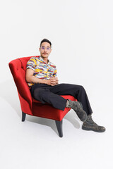 Portrait isolated cutout studio shot Asian vintage classy mustache neck arms hands tattoos male fashion model in casual fashionable classic outfit leather boots sitting on red chair white background