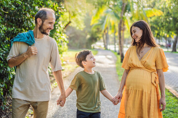 A loving family enjoying a leisurely walk in the park - a radiant pregnant woman after 40, embraced by her husband, and accompanied by their adult teenage son, savoring precious moments together