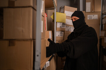 Thief in black gloves take a boxes of goods in a warehouse at night. Security problems in...