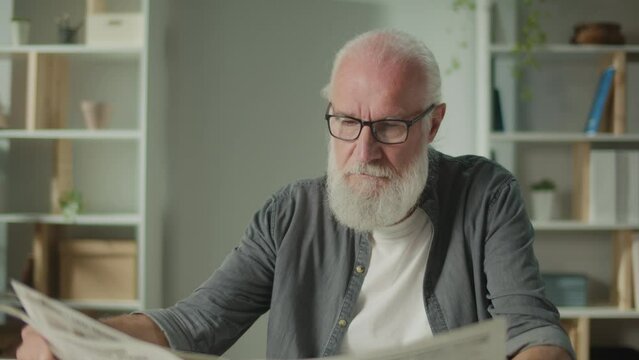 A Serious, Smart Old Man Sits at a Table and Reads a Newspaper.An Elderly Man with a Newspaper Alone at Home, Sees the News and Current Events in the Newspaper.Daily Newspaper Concept