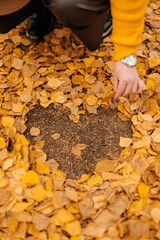 Women's hands, a heart made of leaves. Yellow leaves. Autumn background. September, October.