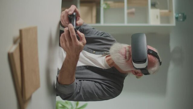 Vertical View.An Old Man in VR Glasses Plays Computer Games With a Joystick, Sitting at the table.A Modern Elderly Man Plays PlayStation. Tech Nostalgia and Generational Divide.