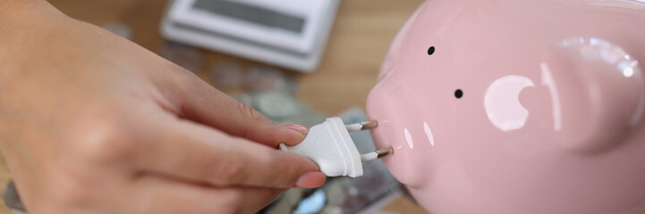 Woman holding power plug and putting on charge pink piggy bank