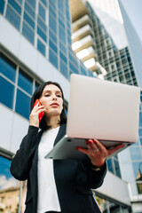 Fototapeta premium Close-up of a business woman standing on a city street. HR manager works outdoors with a laptop near the office.
