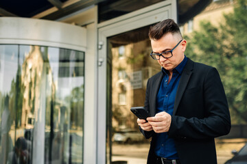 Fototapeta premium Closeup happy handsome male businessman successful on the city street. Portrait of a successful man outdoors. Modern gadgets for lifestyle.