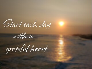 Motivational quote "Start each day with a grateful heart" on nature background. Beautiful sunset at sea horizon, with sun reflection on the water.