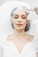 Skin lifting injection. A young woman is receiving a injection in her forehead while lying on a white background. The concept of prolonging youth and cosmetology