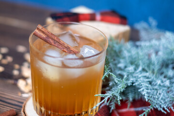 Whiskey cocktail in a glass with ice and a cinnamon stick with a juniper branch in the background...