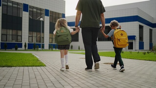Man And Children Walking In Schoolyard, Back View, Little Schoolboy And Schoolgirl Going To Classes