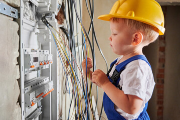 Little boy electrician playing with electrical wires while repairing electric switchboard or...