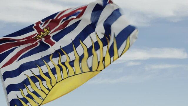 The flag of British Columbia waving in the wind, against a blue sky