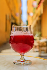 Glass of a raspberry Lambic ale at an outdoor restaurant with a background of blurred buildings in old town or Vieille Ville in Nice, South of France