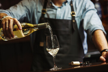 Male sommelier pouring white wine into long-stemmed wineglasses.