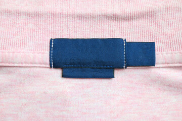 Blank blue laundry care clothes label on pink shirt fabric texture background