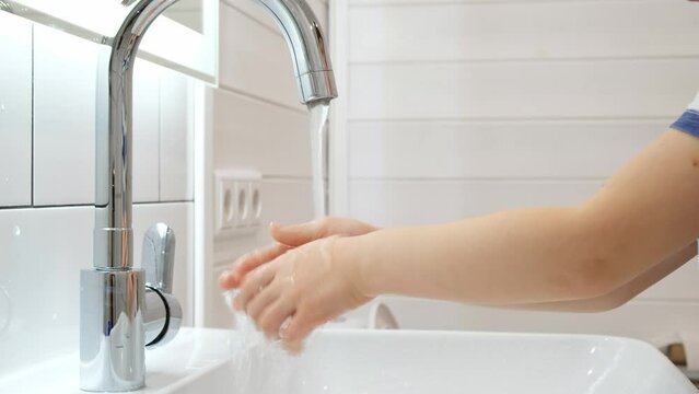 Washing hands of child close-up. The palms of kid under the faucet with water stream. White skin. Caucasian person. Copy space. Clean and hygiene concept. Save health. A good habit. White interior.