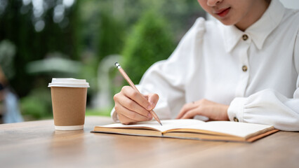 Close-up image of a beautiful Asian woman is keeping a diary while relaxing at an outdoor cafe.