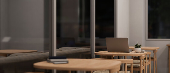 A laptop on a wooden table in a modern, minimalist coffee shop at night.