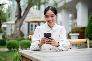 A beautiful Asian woman using her smartphone while sitting at a table in the garden.